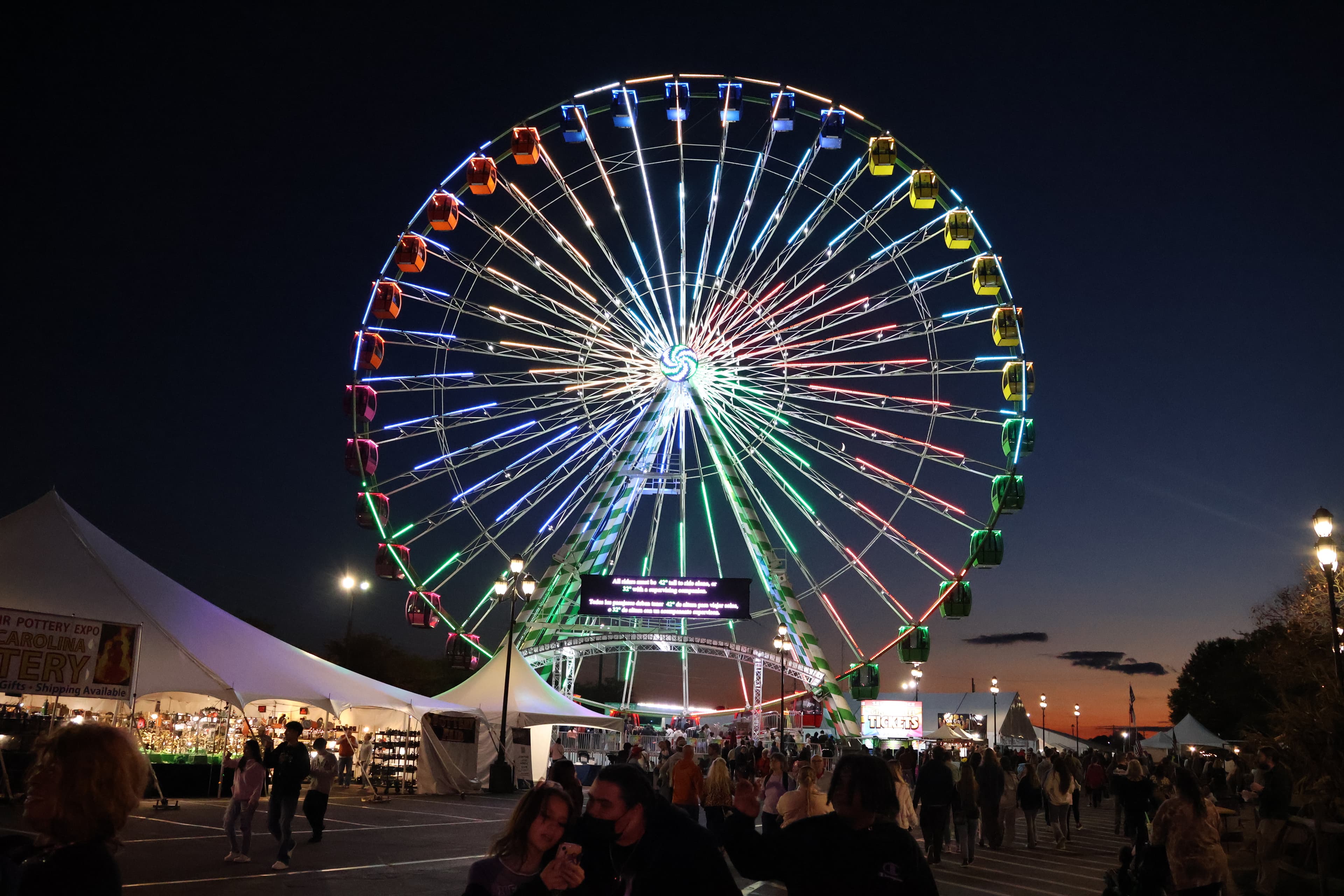 An illuminated Ferris wheel above the crowd at the North Carolina State Fair