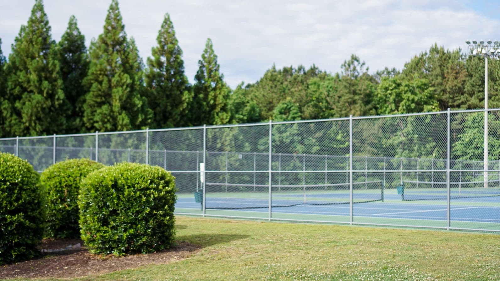Fenced outdoor tennis courts surrounded by trees at J.B. Flaherty Park