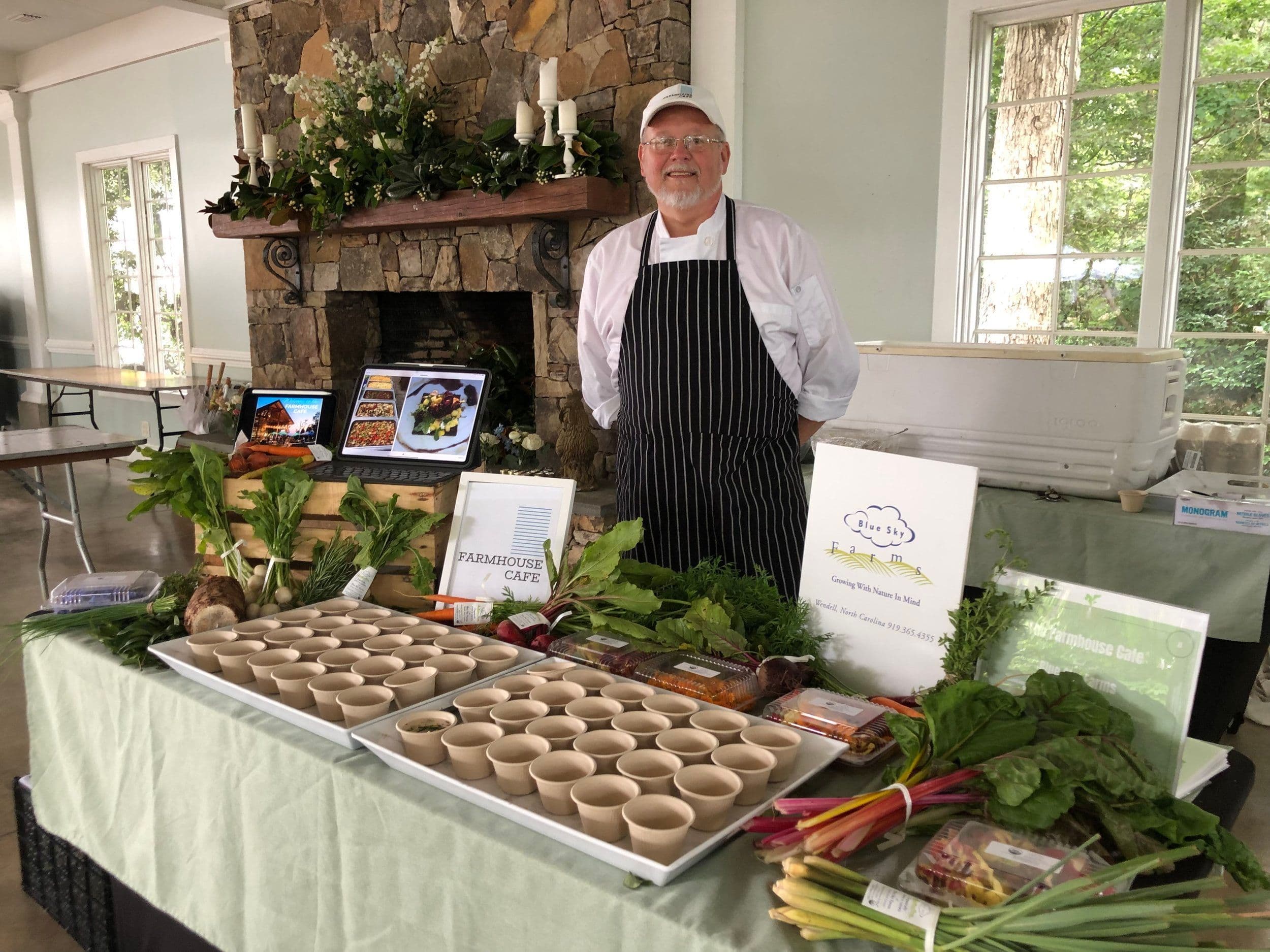 A smiling chef behind a table of small dishes in the Farmhouse Cafe website photo