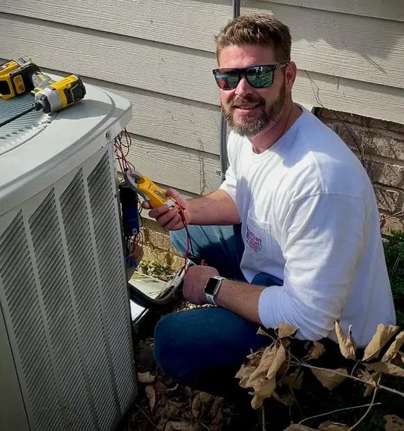 American Comfort Services owner Travis Bennett smiling beside an outdoor HVAC unit