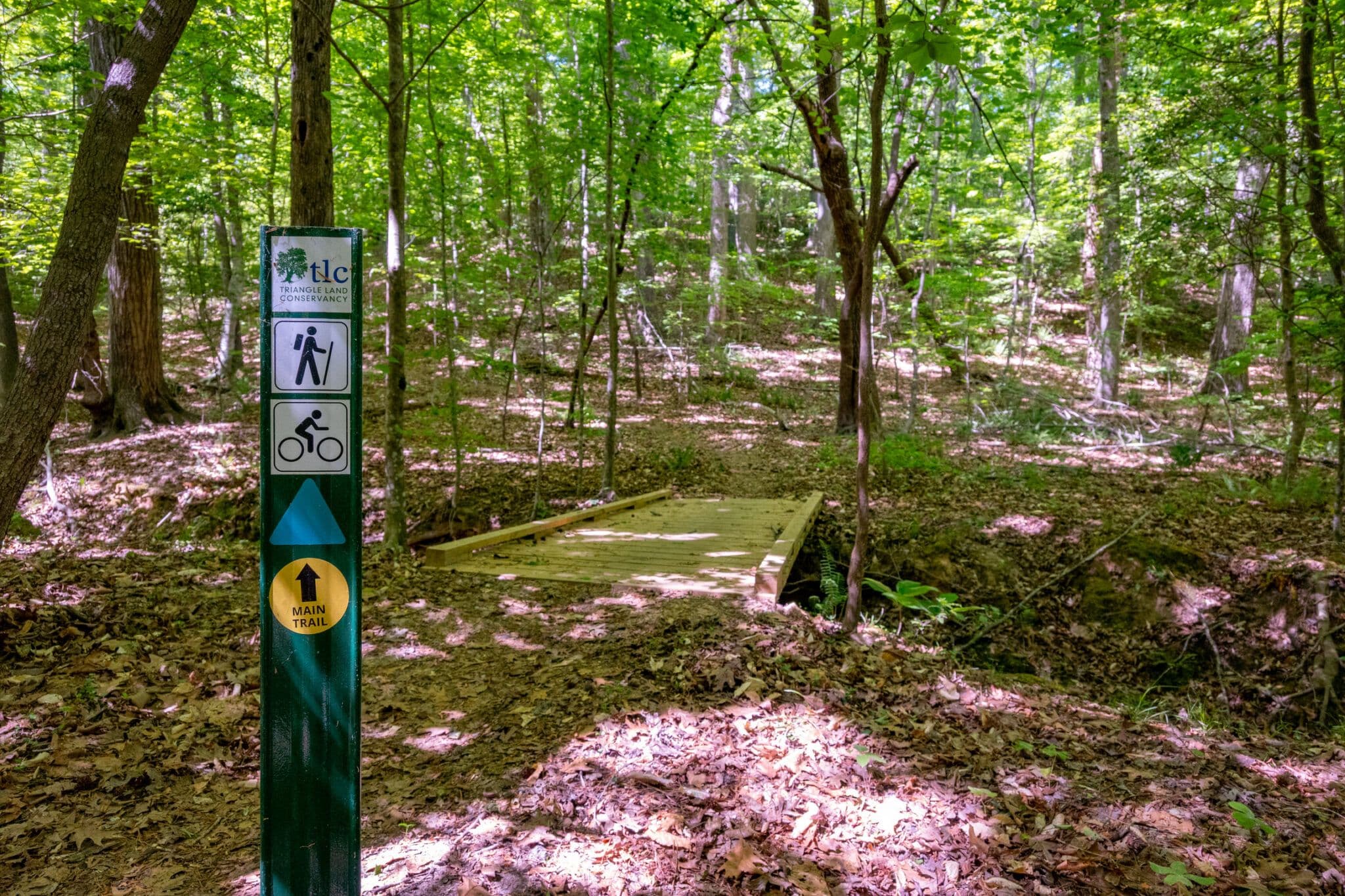 A wooden bridge and hiking and cycling trail sign in the woods at Old Creedmoor Nature Preserve
